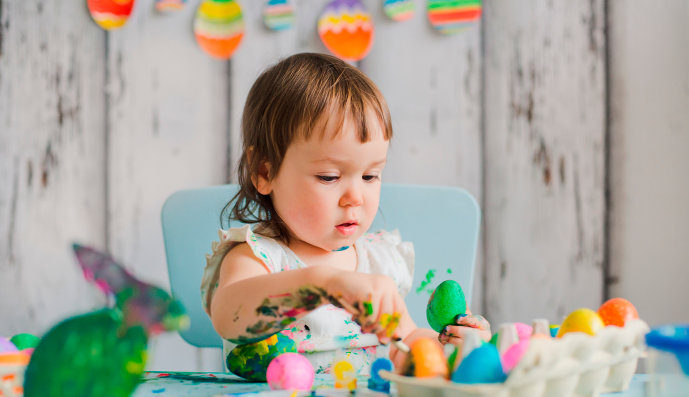 Foto: Kleines Mädchen sitzt am Tisch und bemalt Ostereier.