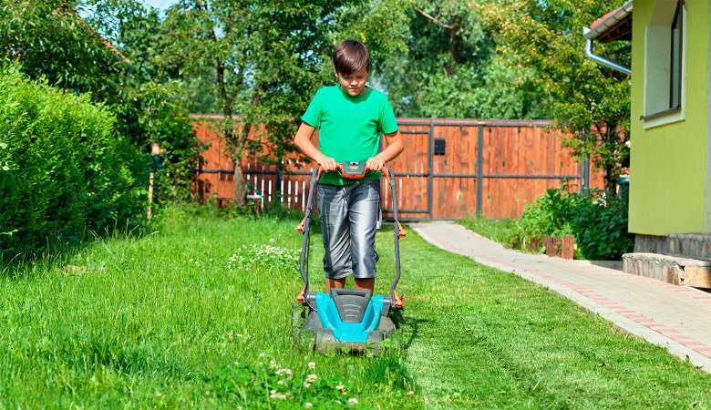 Foto: Junge, der mit einem Rasenmäher den Rasen mäht