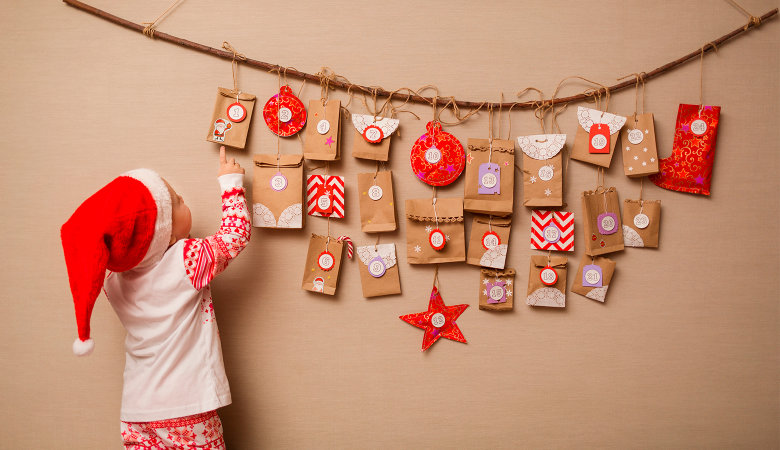 Foto: Kleines Kind mit Nikolausmütze auf dem Kopf steht an einem Adventskalender und zeigt auf das erste Geschenk