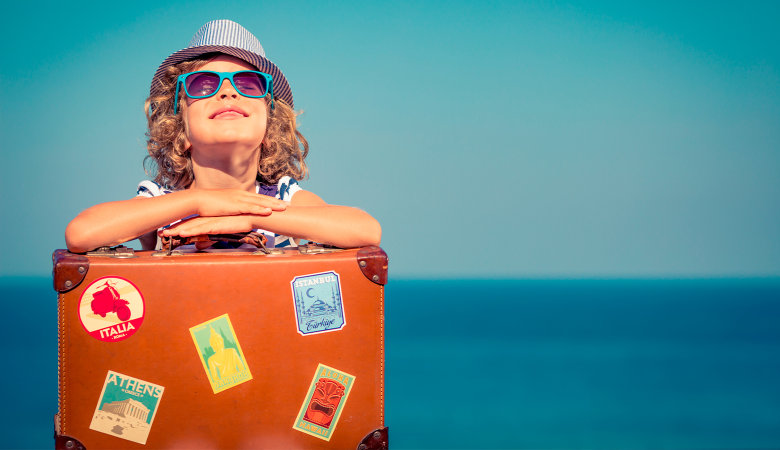 Foto: Kleines Mädchen mit Sonnenhut und Sonnenbrille hat Arme auf einen Reisekoffer aufgestützt
