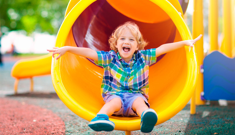 Foto: Fröhlicher kleiner Junge auf dem Spielplatz rutsch in einer Röhre.