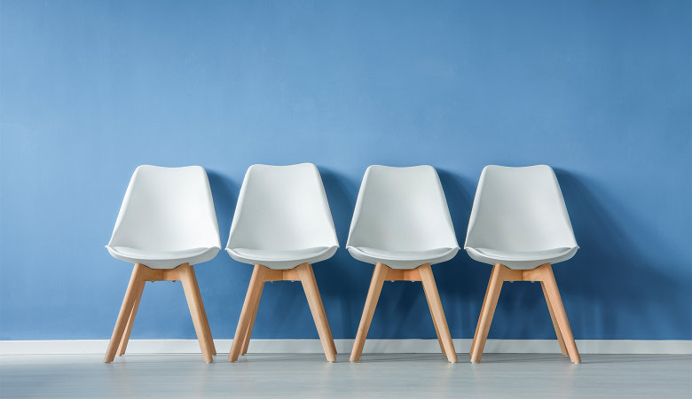 Foto: Vier aufgereihte leere Stühle an einer Wand
