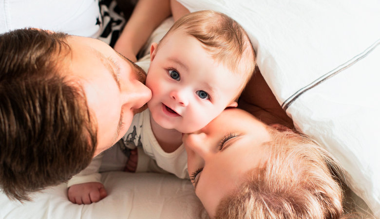 Foto: Junge Familie liegt im Bett und küsst ihr Baby