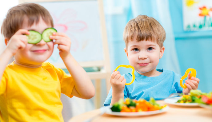 Foto: Zwei Jungs sitzen in der Küche und essen Gemüse.