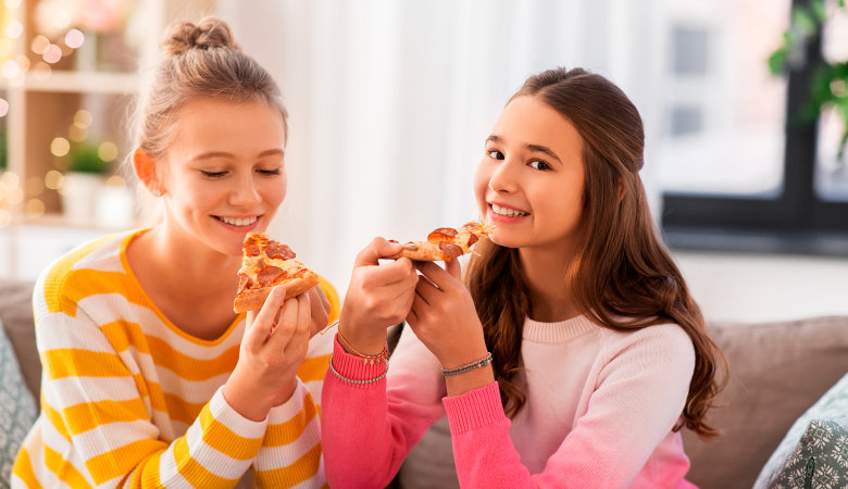 Foto: Zwei glückliche Teenagermädchen essen zu Hause Pizza