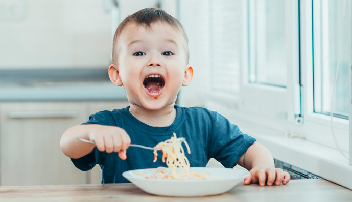 Foto: Kleiner Junge sitzt am Tisch und isst eigenständig Spaghetti 