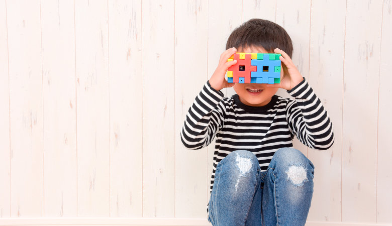 Foto: Kleiner Junge lehnt gehockt an einer Wand und schaut durch zwei Spielwürfel, die er sich vor die Augen hält.