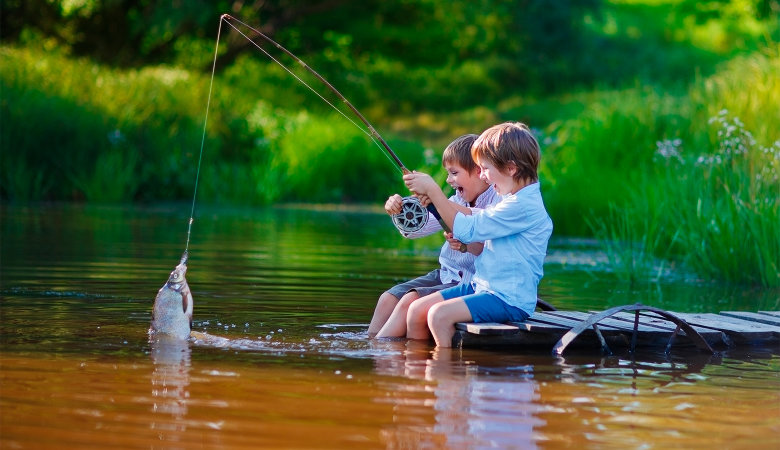 Foto: Zwei kleine Jungen angeln an einem Steg einen Fisch aus einem Teich