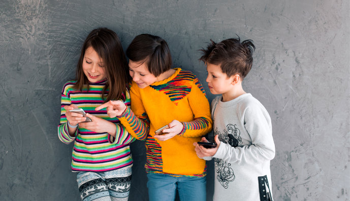Foto: Drei Kinder stehen lachend mit ihren Smartphones zusammen.