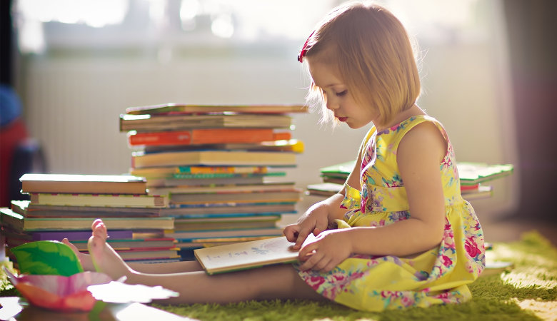 Foto: kleines Mädchen sitzt auf dem Fußboden und liest ein Kinderbuch