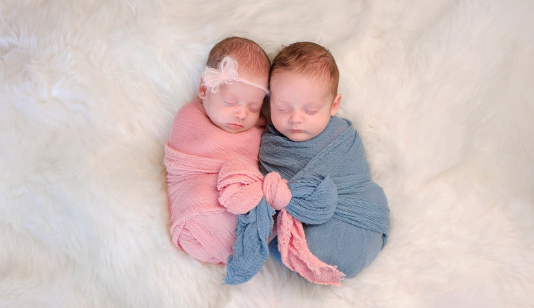 Foto: Zwei Monate alte Babys, ein Junge und ein Mädchen, eingewickelt in Tücher, liegen nebeneinander auf einer Decke.
