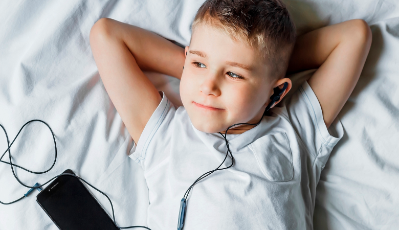 Foto: Junge liegt auf dem Bett und hört Musik mit Kopfhörer und Smartphone 