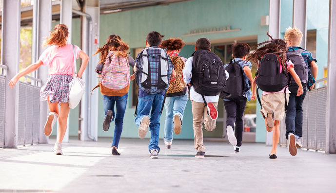 Foto: Acht Grundschulkinder laufen mit Schulranzen auf dem Rücken einen Gang entlang.