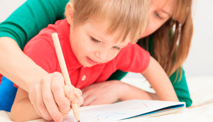 Foto: Mutter und Kind halten zusammen einen Zeichenstift und schreiben auf ein Blatt Papier die Buchstaben A B C