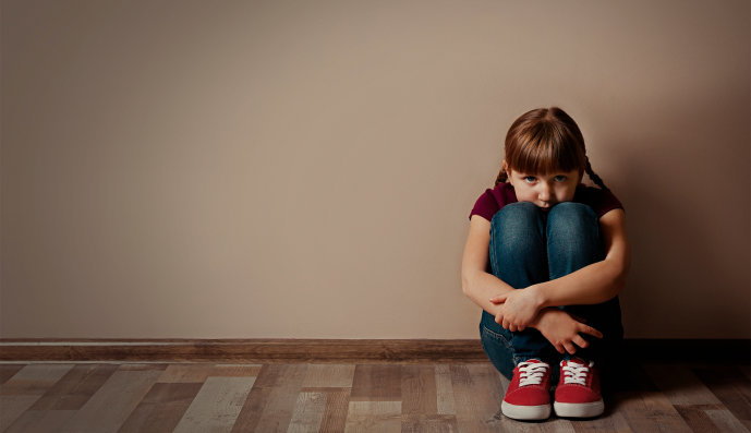 Foto: Trauriges Mädchen sitzt mit angewinkelten Beinen am Fußboden an eine Wand gelehnt