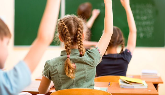Foto: Schulkinder im Klassenzimmer mit erhobenen Händen.