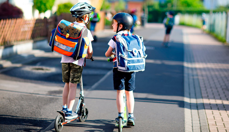 Foto: Zwei Schuljungen mit Roller und Schulrucksack auf dem Weg zur Schule.
