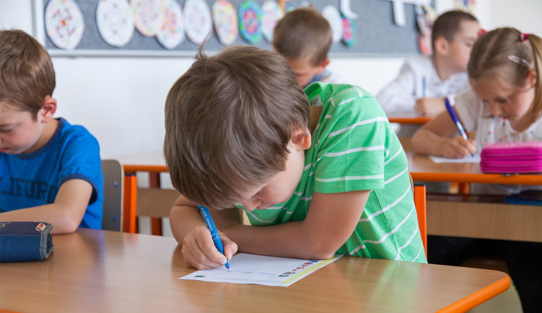 Foto: Fünf Schulkinder im Klassenzimmer, die auf ein Blatt Papier schreiben